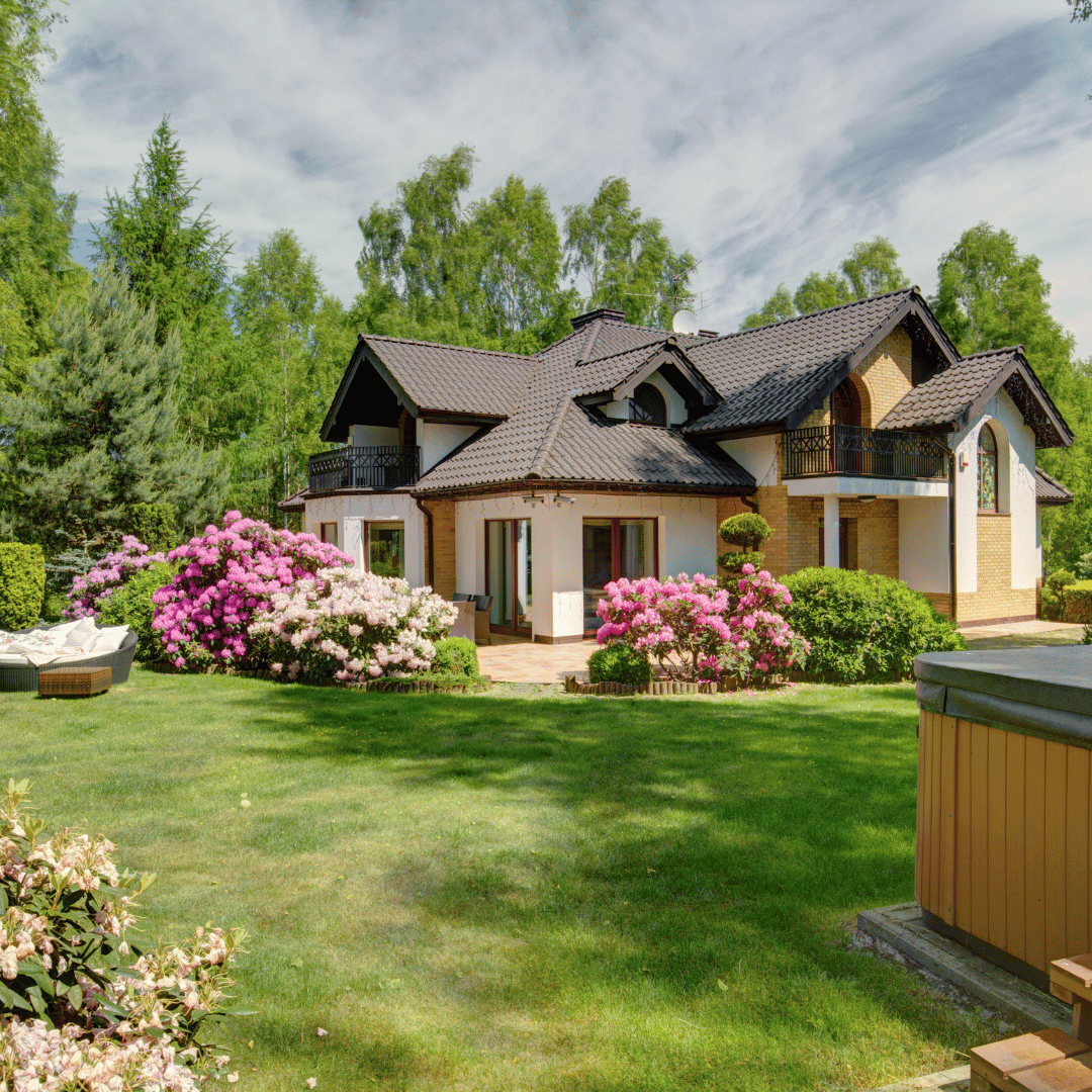 Lush backyard garden in Boston featuring vibrant blooming pink and white rhododendrons, a perfectly manicured lawn, and mature trees surrounding a traditional estate.
