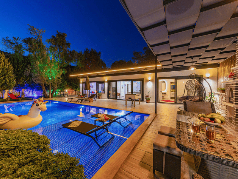 Modern backyard hardscaping featuring a large stone tile patio, an integrated outdoor kitchen area with a stone oven, and a luxury swimming pool installation.