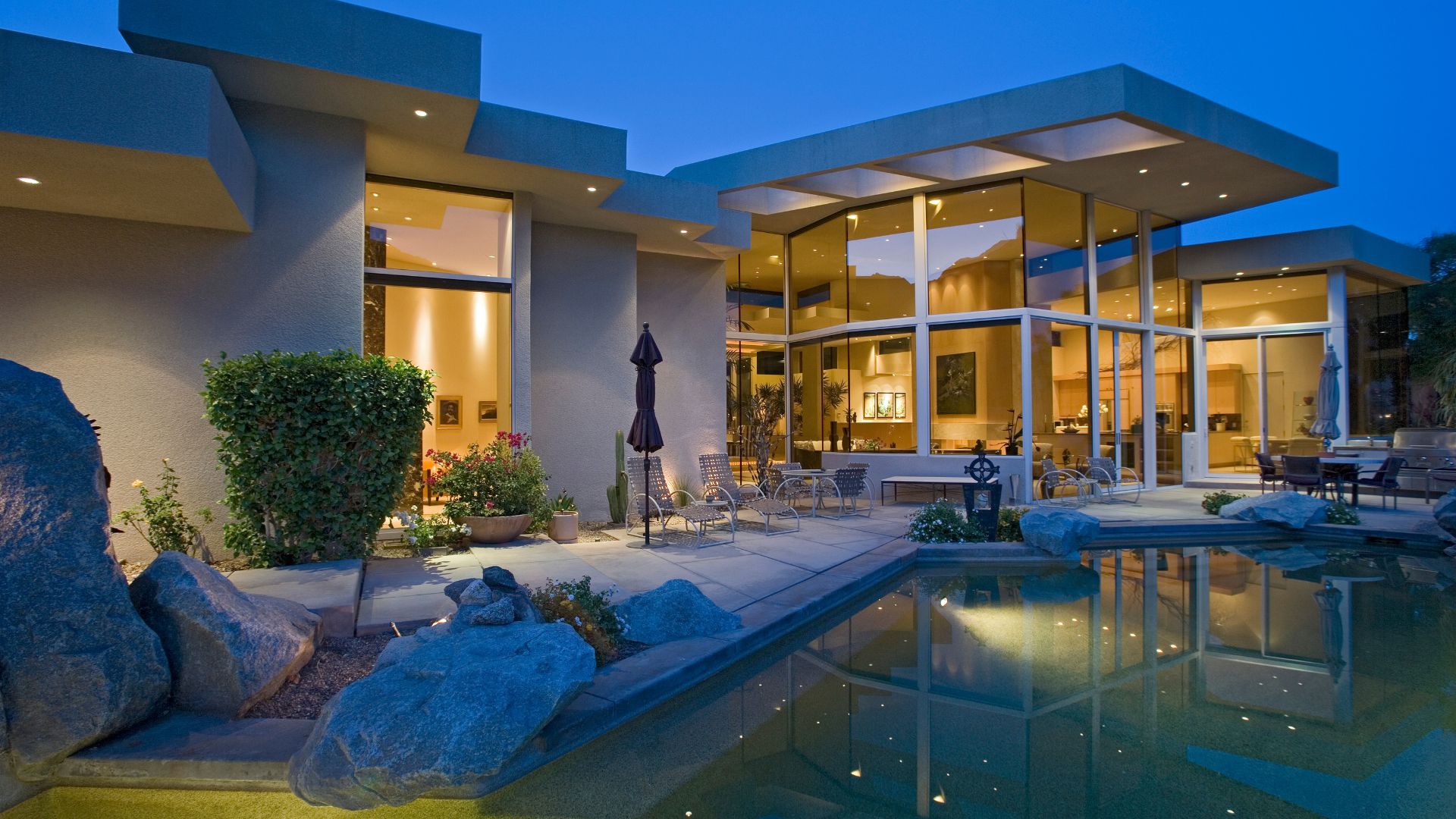 Modern luxury pool design in Boston featuring a custom stone patio, integrated natural rock features, and a seamless transition from the home's architecture to the outdoor living space.